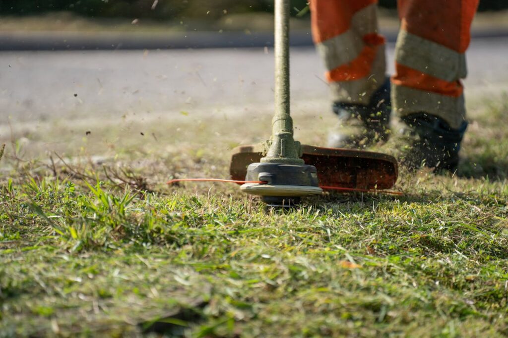 pexels-photo-11400235 Close-up of a person trimming grass with a power tool outdoors.